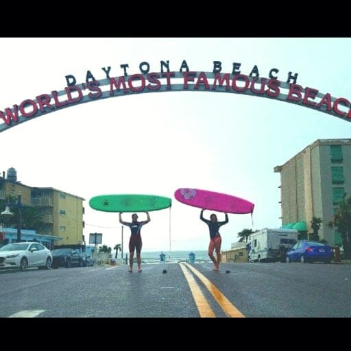 Surfers carrying boards under the Daytona Beach arch